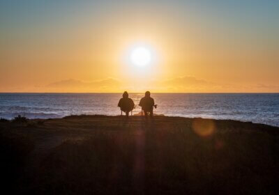 The silhouettes of two people sitting in chairs overlooking the sea watching a sunrise or sunset